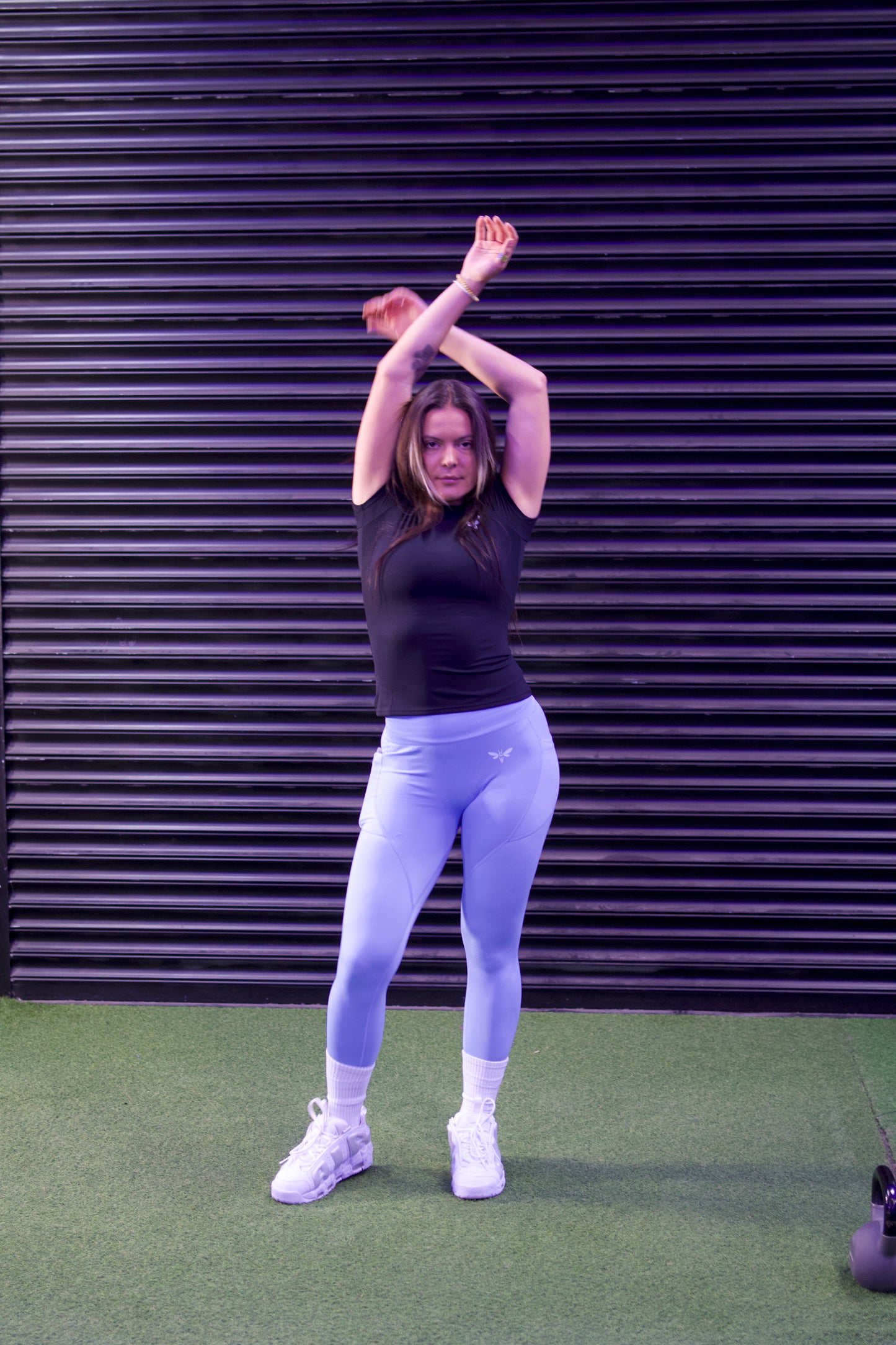 Person stretching arms above head in front of a dark metallic door and wearing Light Blue balancewise leggings