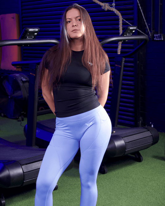 Woman in black top and Person wearing  Light Blue balancewise leggings with a balancewise logo posing in a gym setting