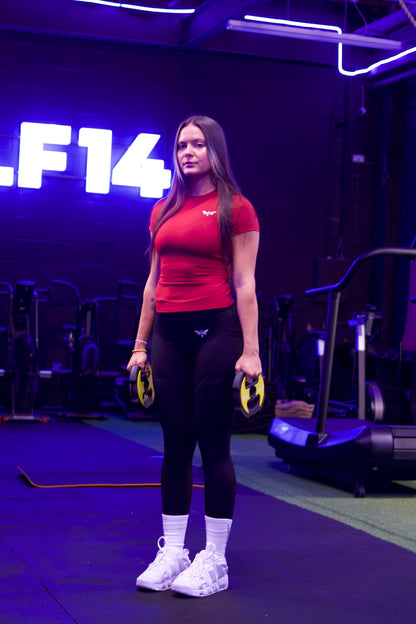 Woman flexing her arm in a red Balancewise gym shirt with visible logo